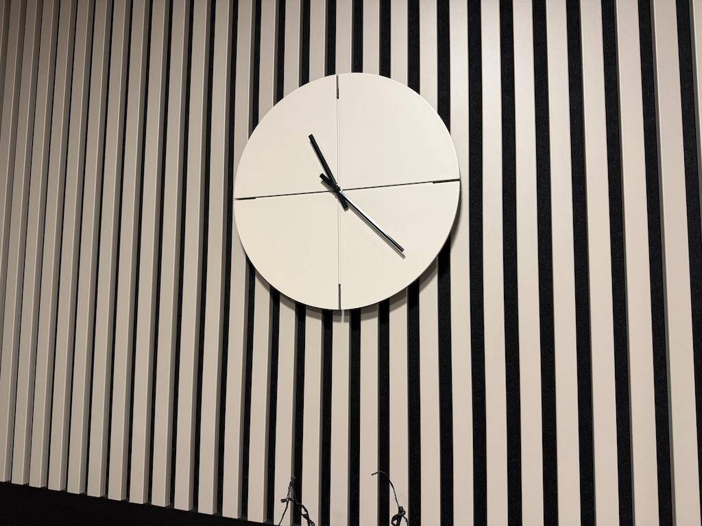 Eine moderne weiße Wanduhr an einer dekorativen Wandverkleidung mit vertikalen Lamellen.
