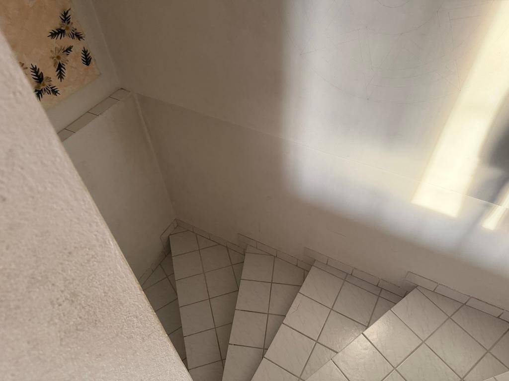 Blick von oben auf eine geflieste Treppe mit weißen Wänden und schlichtem Design.