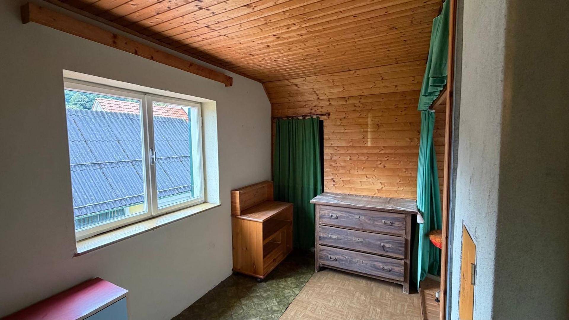 Gemütliches Zimmer mit Holzvertäfelung an Decke und Wänden, ausgestattet mit einem Fenster und Möbeln.