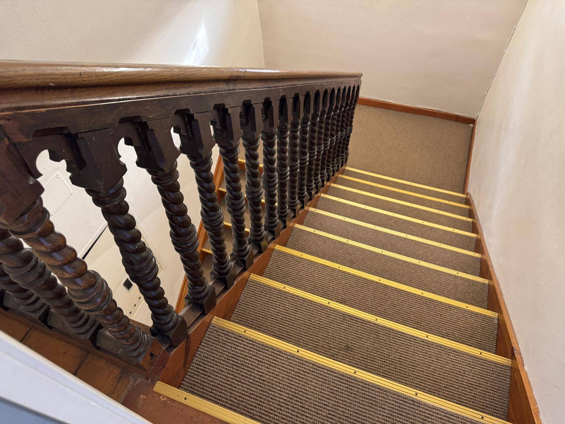 Treppenhaus mit Holztreppe, Teppichläufern und einem verzierten Holzgeländer.