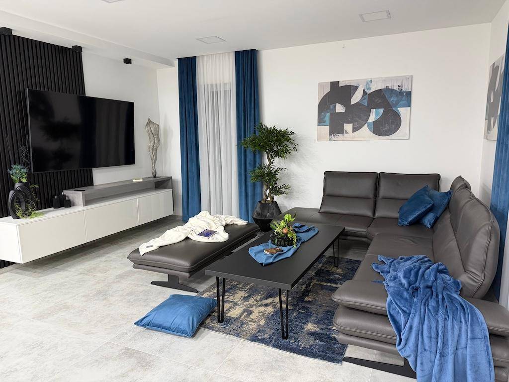 Modernes Wohnzimmer mit großem Ecksofa, Fliesenboden und stilvoller Dekoration in Blau- und Grautönen.