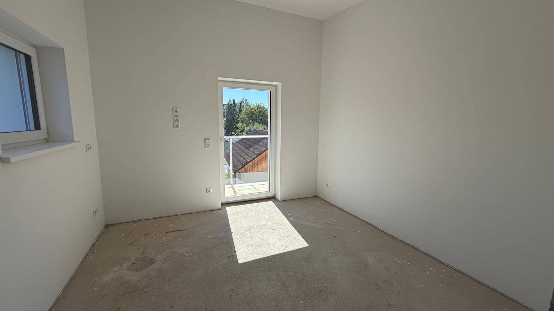Unfertiger Raum mit viel Tageslicht durch eine Tür und ein Fenster, bereit für den Ausbau.