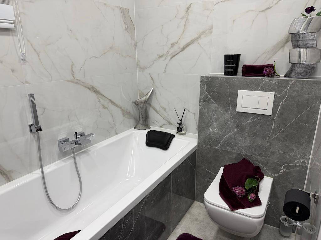 Elegantes Badezimmer mit Badewanne, wandhängendem WC und luxuriösen Marmorfliesen in Grau und Weiß.