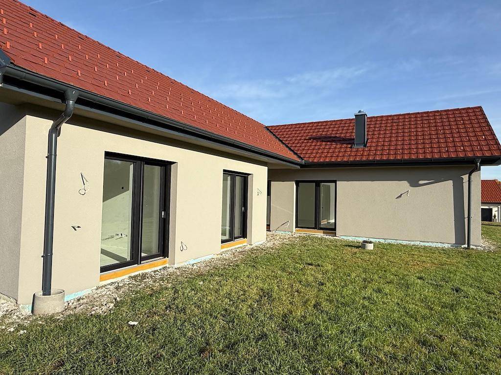 Hausfassade des Neubaus mit großen Fenstertüren und einer unfertigen Rasenfläche im Vordergrund.