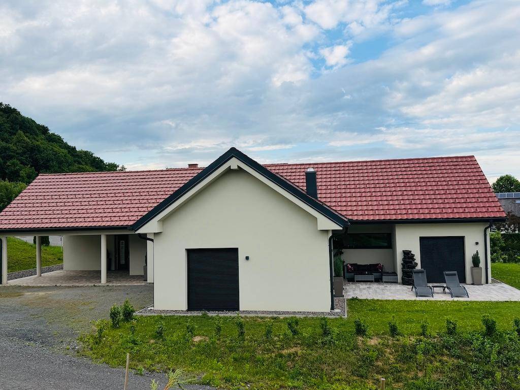 Modernes Einfamilienhaus mit rotem Ziegeldach, weißer Fassade und integriertem Carport.
