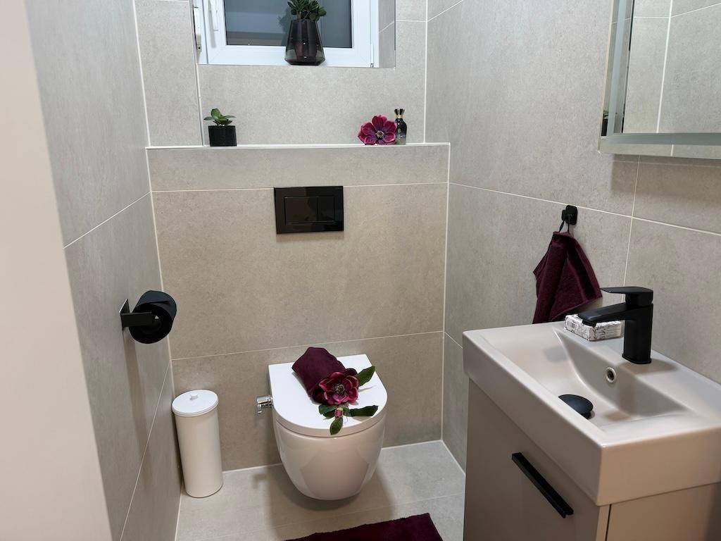 Modernes Gäste-WC mit hellen Fliesen, wandhängendem WC und kleinem Waschbecken.