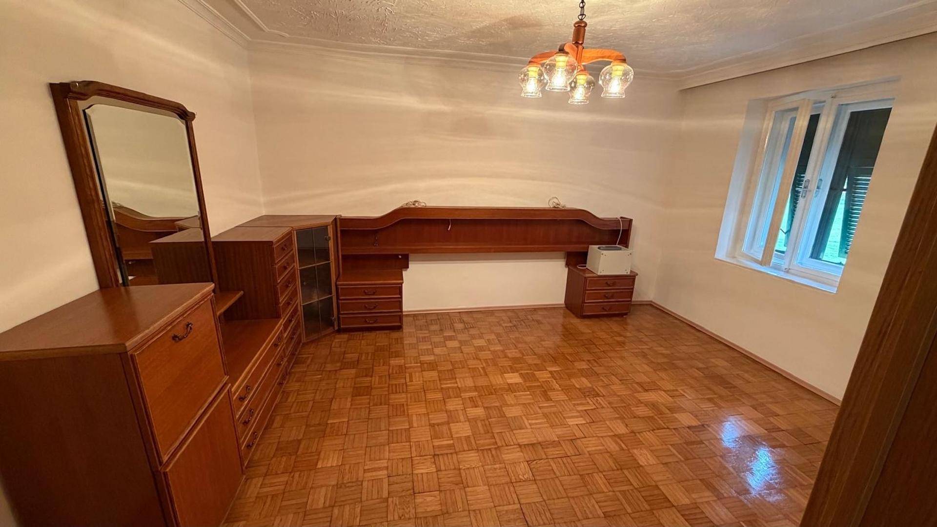 Schlafzimmer mit Parkettboden, Fenster und einem großen Holzschrank mit Spiegel.
