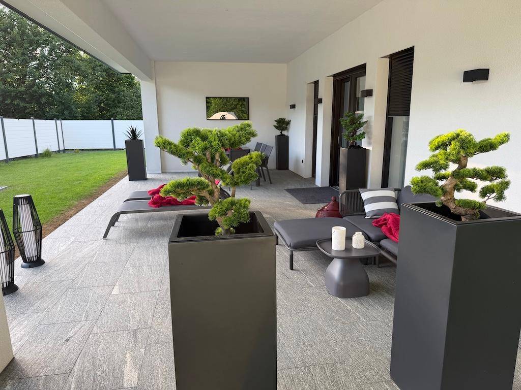 Geräumige Terrasse mit modernen Lounge-Möbeln, Zierpflanzen und Blick in den Garten.