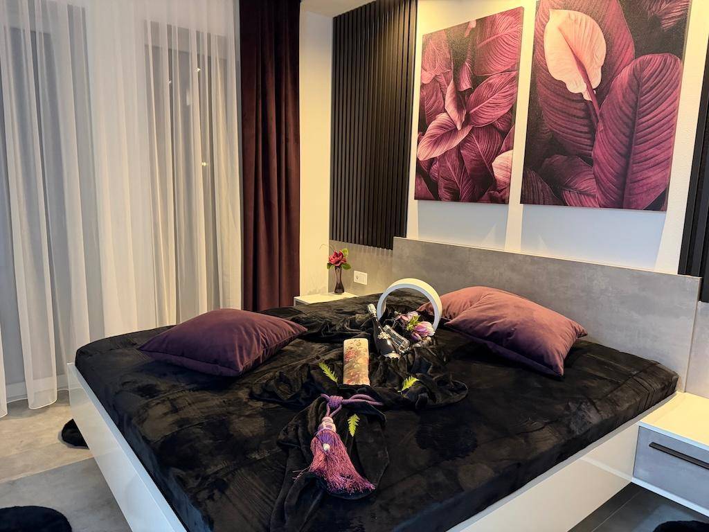 Modernes Schlafzimmer mit dunklem Bett, lila Akzenten und stilvoller Beleuchtung für eine angenehme Atmosphäre.