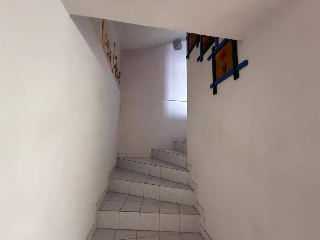 Schmale Treppe mit weißen Fliesen und Wänden, die in ein Obergeschoss führt.