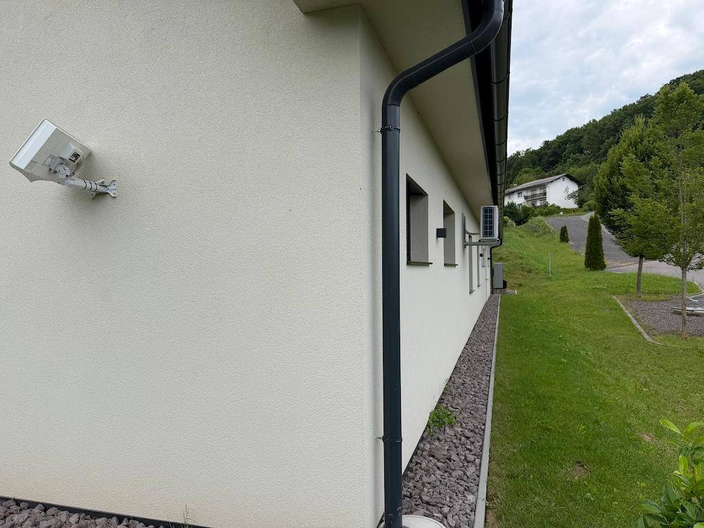 Seitenansicht des Hauses mit weißer Fassade, kleinen Fenstern und installierter Klimaanlage.