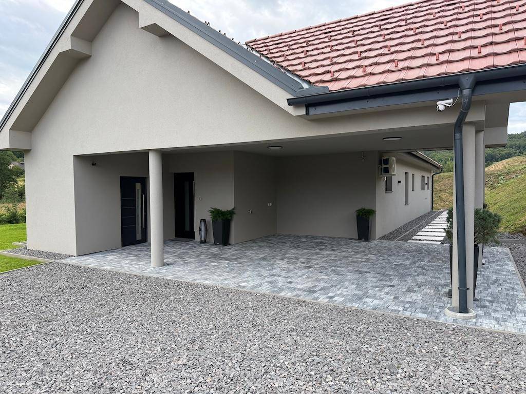 Eingangsbereich des Hauses mit Carport, gepflastertem Vorplatz, Überwachungskamera und Klimaanlage.