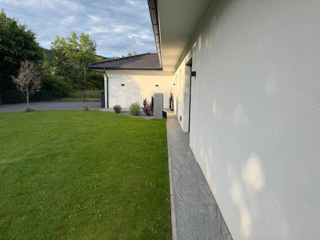 Seitenansicht des Hauses mit gepflegtem Rasen und einem schmalen Steinweg entlang der Fassade.