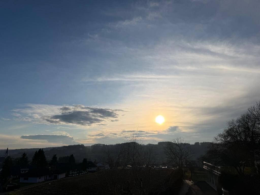 Malerischer Sonnenuntergang über einer hügeligen Landschaft mit Bäumen und weitem Himmel.