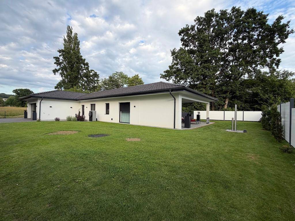 Modernes Einfamilienhaus mit weitläufigem Rasen und großer überdachter Terrasse, umgeben von viel Grün.