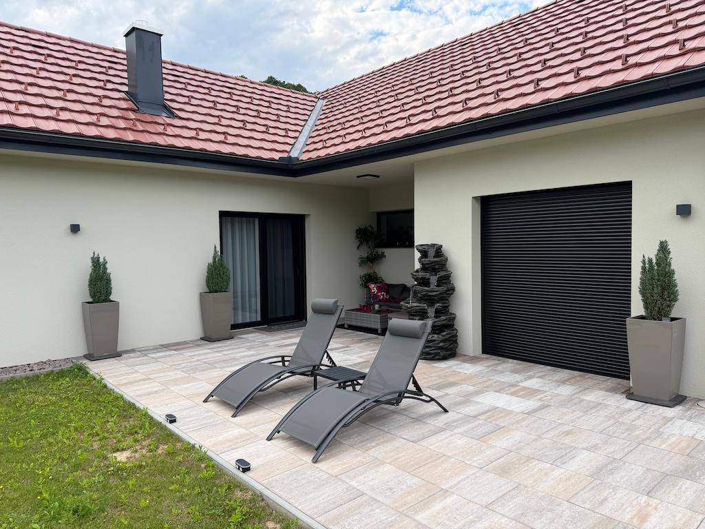 Geräumige, geflieste Terrasse mit zwei Sonnenliegen und einem dekorativen Wasserfall, perfekt für sonnige Tage.