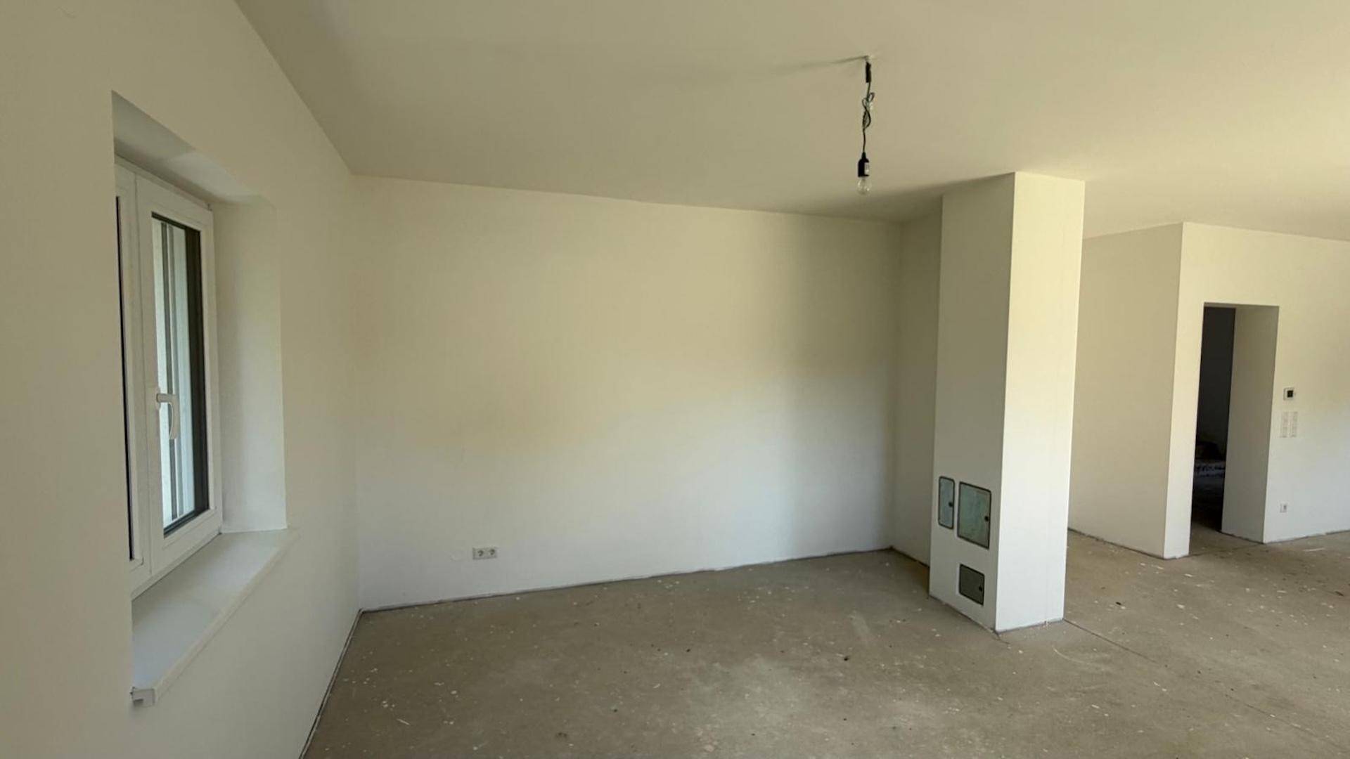 Geräumiger Wohnbereich im Rohbau mit einer Säule, die einen Kamin beherbergen könnte.