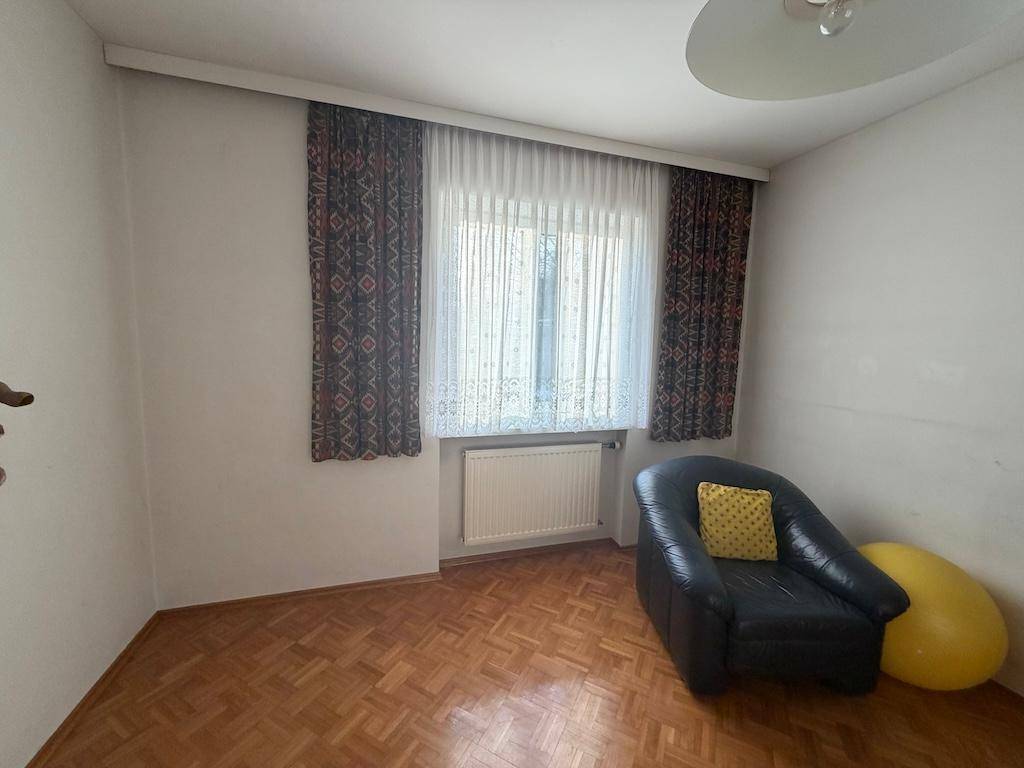 Kleines Zimmer mit Parkettboden, Fenster und einem einzelnen Sessel, gemütlich eingerichtet.