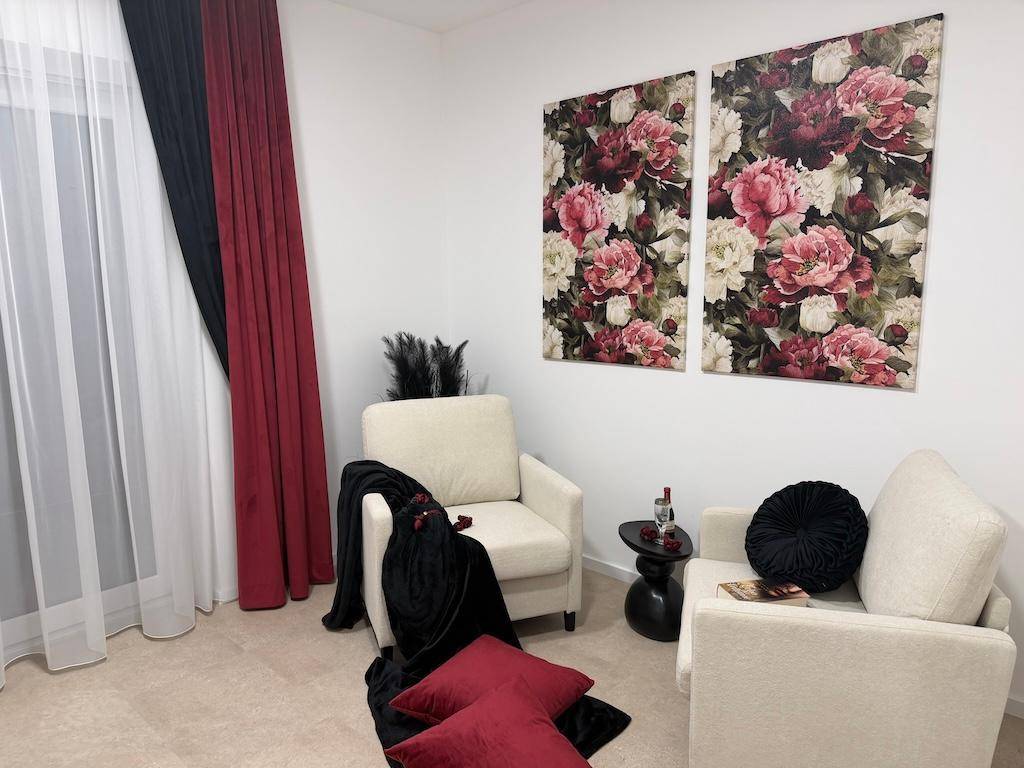Heller Wohnbereich mit bequemen Sesseln, floralen Bildern und eleganten Vorhängen am Fenster.