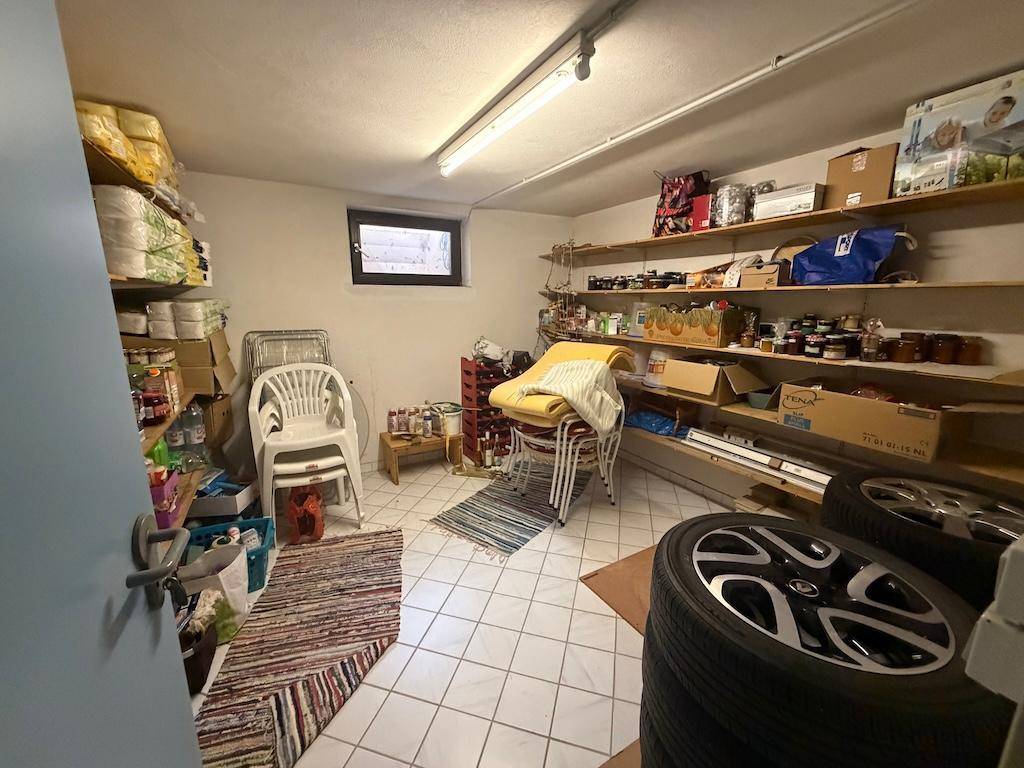 Geräumiger Abstellraum im Keller mit Regalen, Stühlen und gelagerten Reifen.