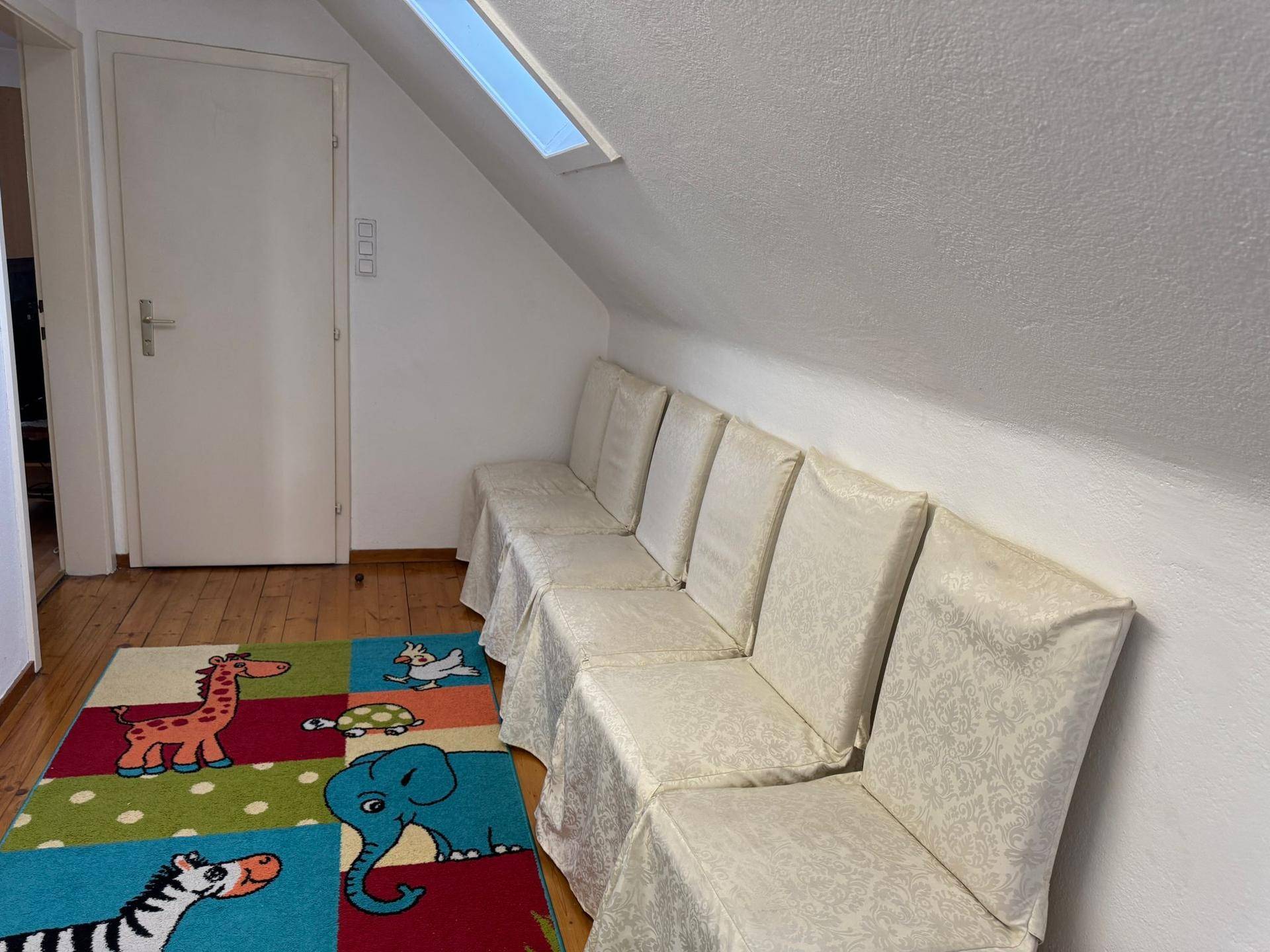 Dachgeschossraum mit schrägen Wänden, einem Dachfenster und einer Reihe von Stühlen.