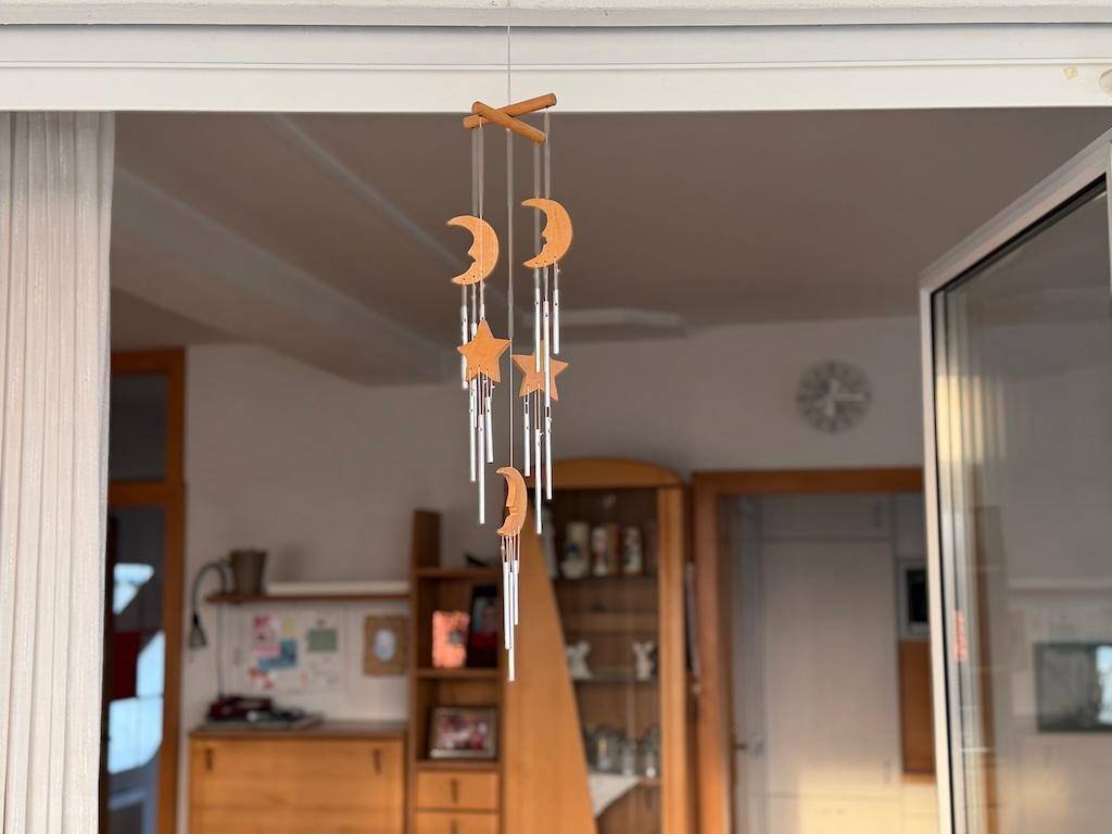 Windspiel mit Mond- und Sternmotiven hängt im Türrahmen, im Hintergrund ein Wohnbereich.