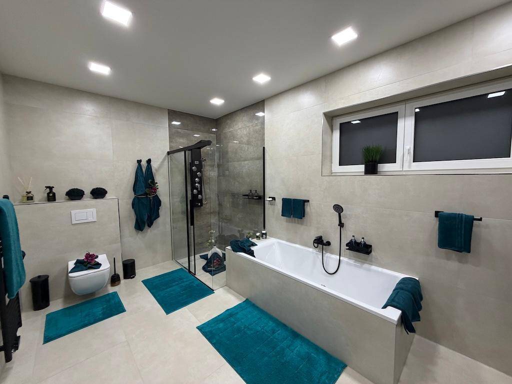 Geräumiges Badezimmer mit moderner Badewanne, begehbarer Dusche und Fenster für Tageslicht.