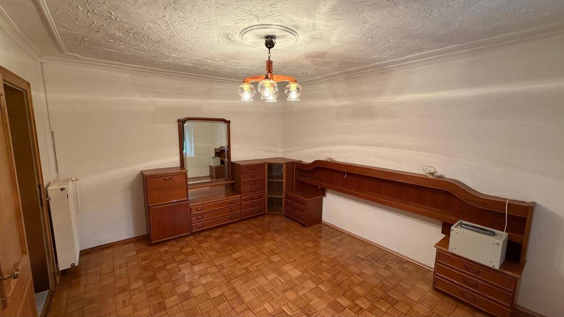 Geräumiges Schlafzimmer mit Holzparkett und traditionellen Holzmöbeln, inklusive Spiegel und Kommoden.