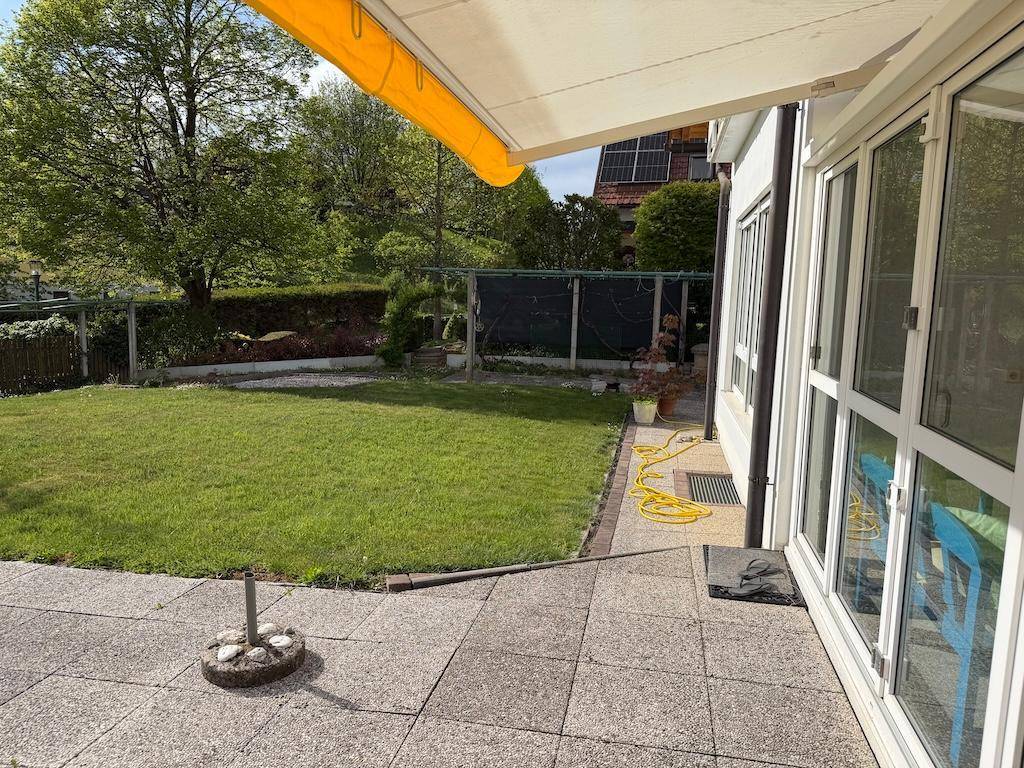 Große gepflasterte Terrasse mit Rasenfläche und ausfahrbarer Markise am Haus.