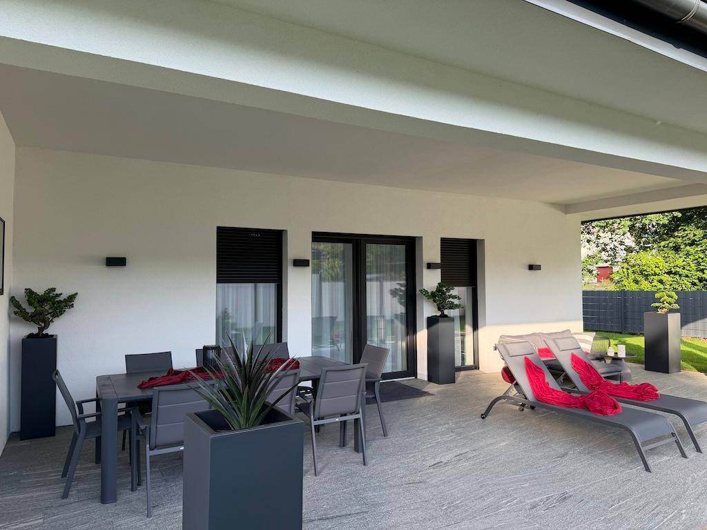 Großzügige überdachte Terrasse mit modernen Gartenmöbeln und Liegestühlen, ideal zum Entspannen im Freien.
