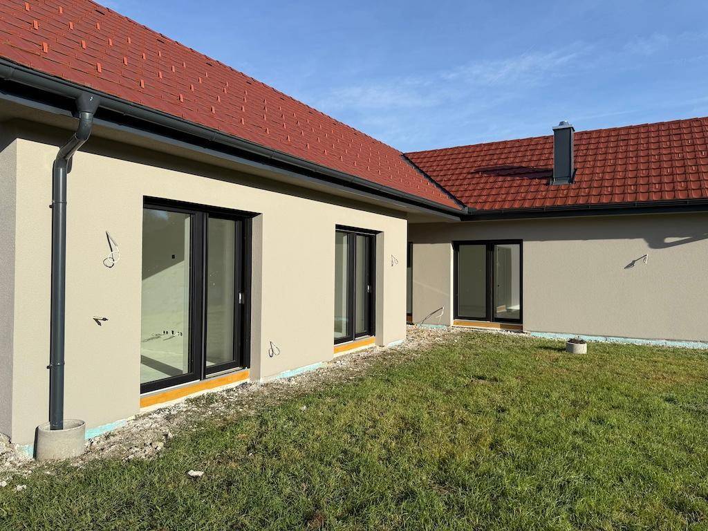 Rückseite des Neubaus mit großen Fenstertüren und einer kleinen Rasenfläche, bereit zur Gestaltung.