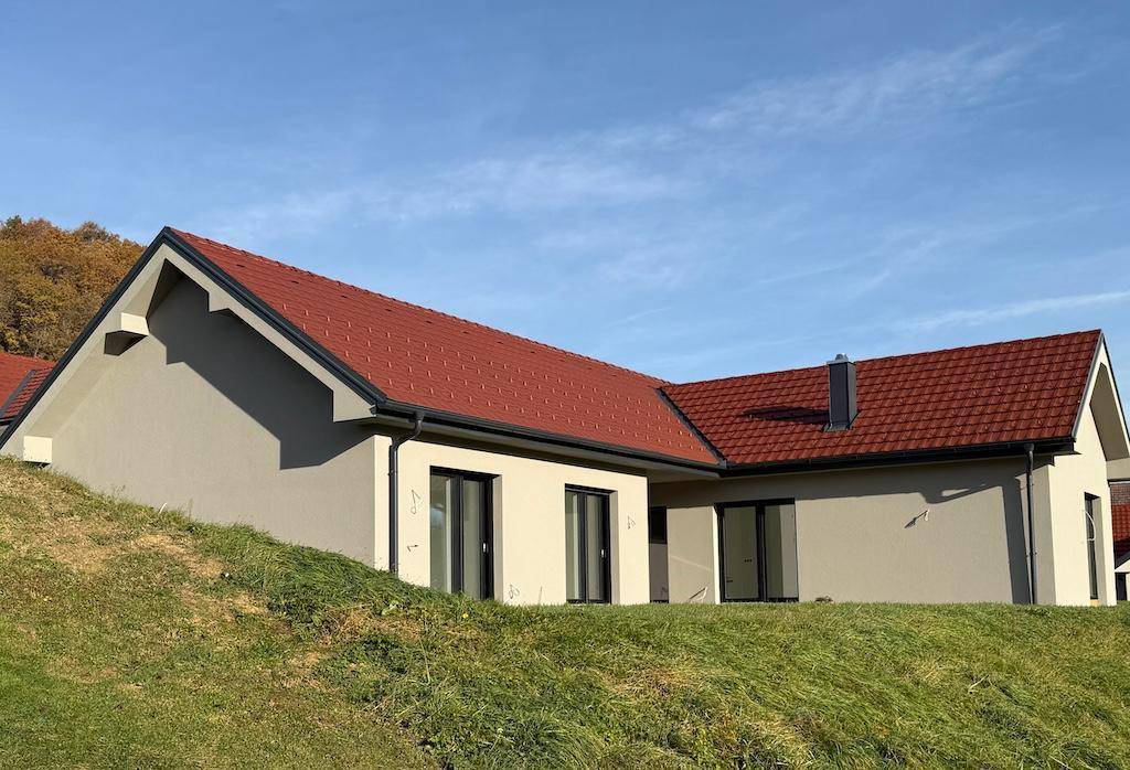 Modernes Einfamilienhaus mit heller Putzfassade und rotem Dach, umgeben von einer grünen Wiese.