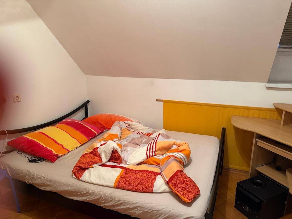 Schlafzimmer mit Einzelbett, Schreibtisch und farbigen Kissen unter einer Dachschräge.