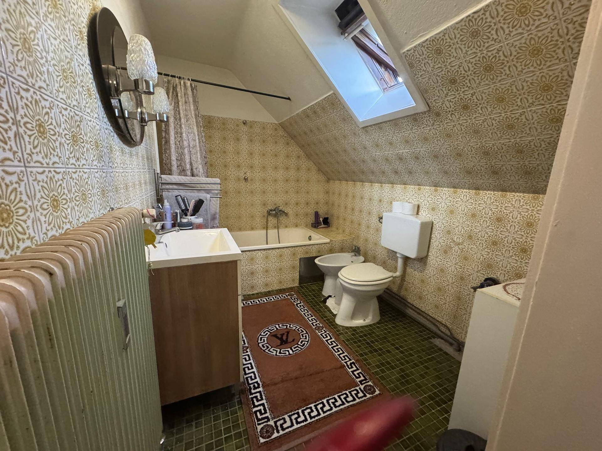 Badezimmer im Dachgeschoss mit Badewanne, Bidet, WC und gemusterten Fliesen.