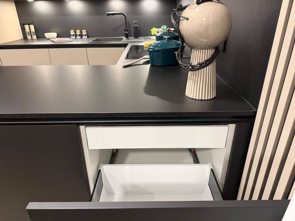 Moderne Küchenzeile mit dunkler Arbeitsplatte und einem geöffneten Schubfach, minimalistisches Design.