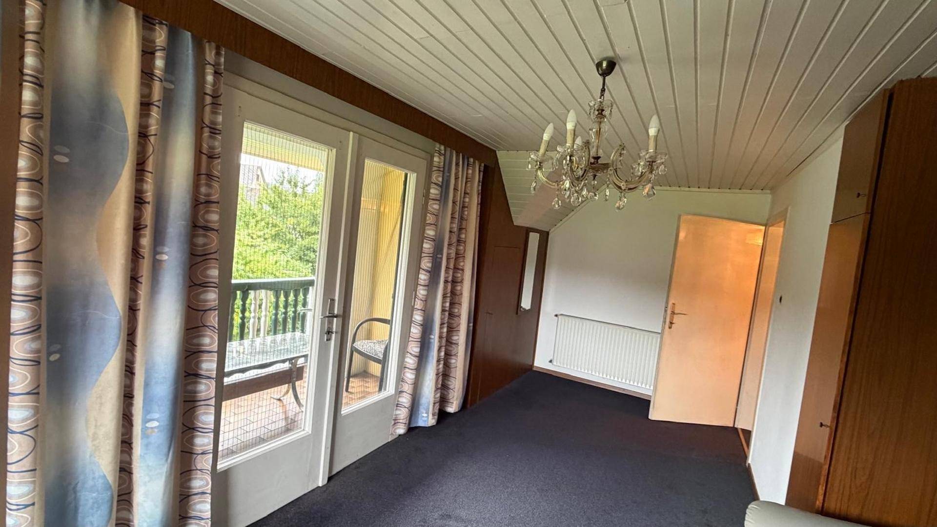Schlafzimmer mit Teppichboden, Holzdecke, Kronleuchter und Zugang zu einem kleinen Balkon.