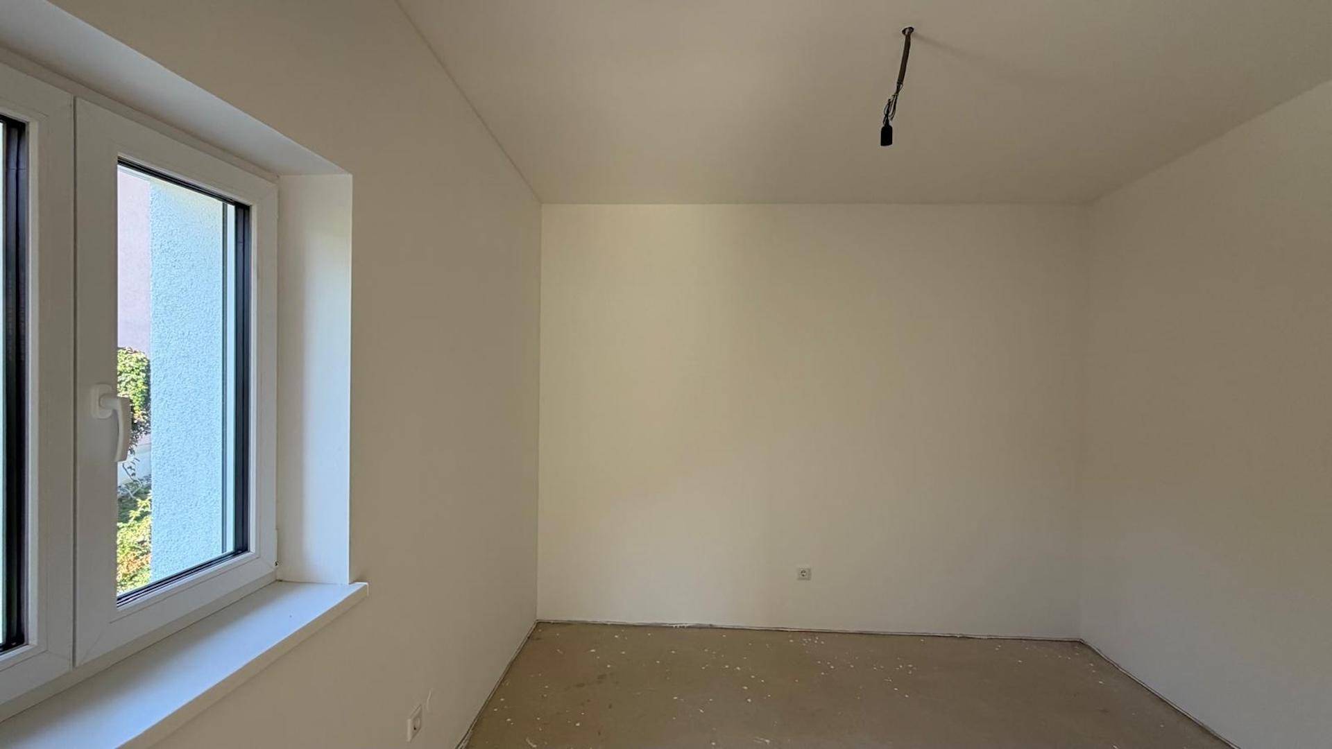 Unfertiges Zimmer mit weiß gestrichenen Wänden und einem Fenster, bereit für den Bodenbelag.