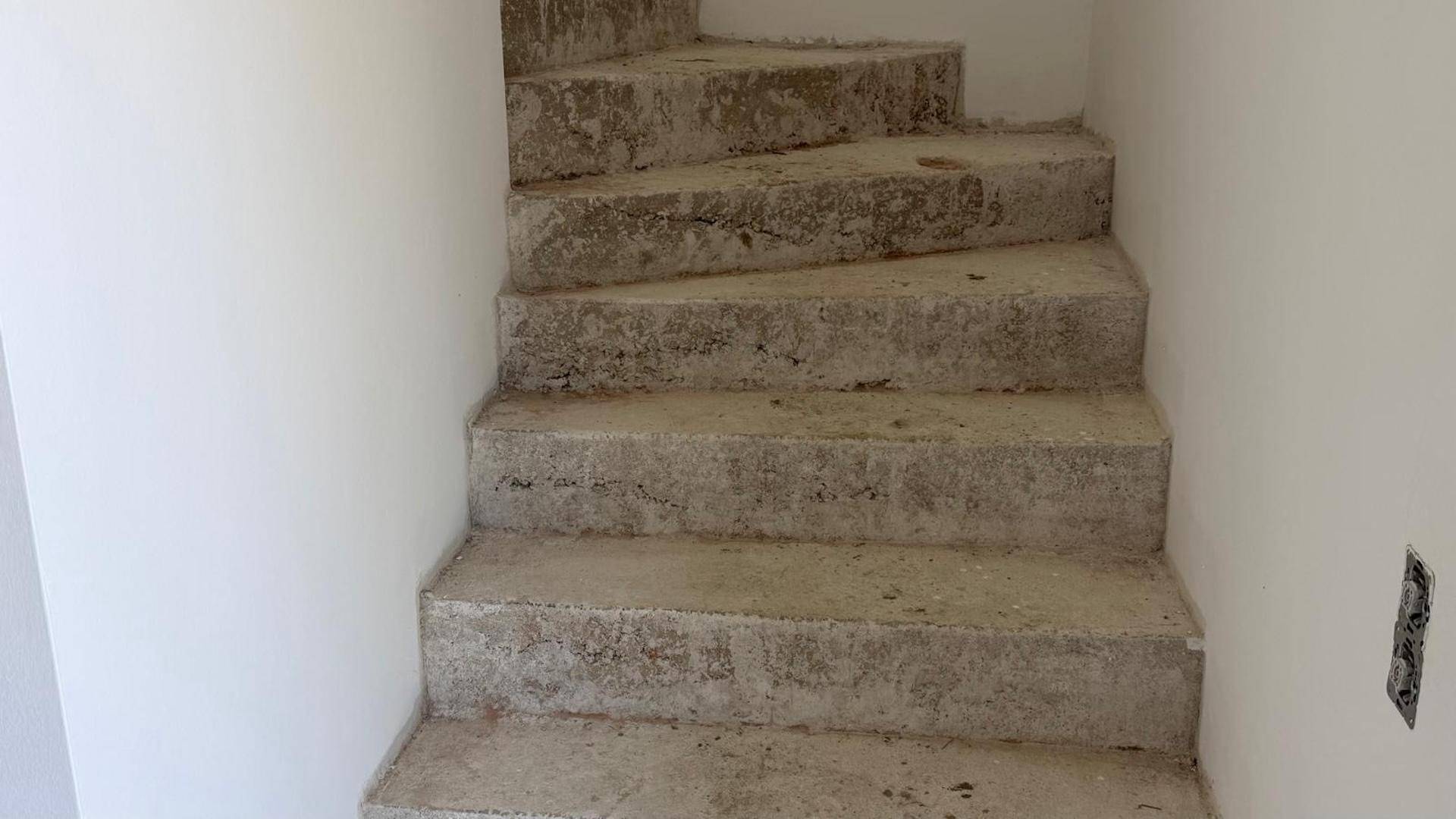 Rohe Betontreppe in einem Neubau, die auf die Fertigstellung und den Einbau des Geländers wartet.