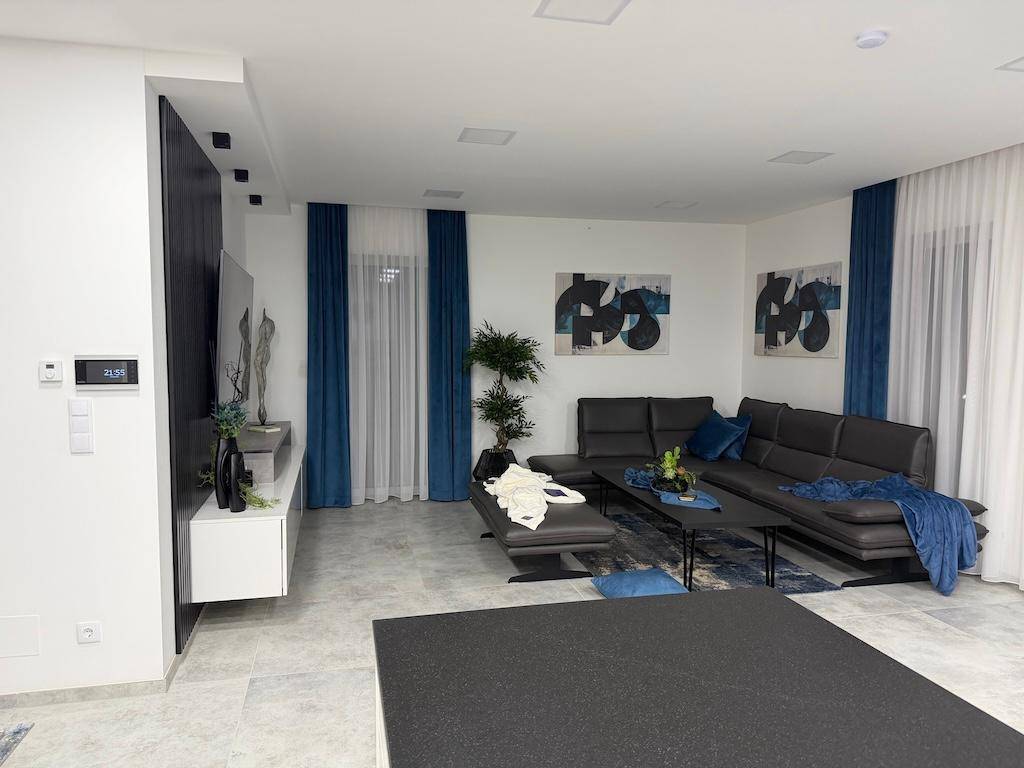 Geräumiges Wohnzimmer mit modernem Ecksofa, großem Fernseher und blauen Vorhängen, hell und einladend.