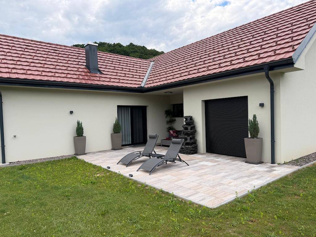 Helle, geflieste Terrasse mit Sonnenliegen und einem dekorativen Wasserfall, umgeben von Rasenfläche.