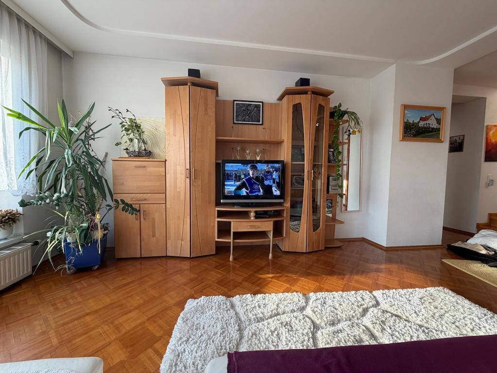Wohnzimmer mit Parkettboden, TV-Möbeln und Zimmerpflanzen, hell durch große Fenster.