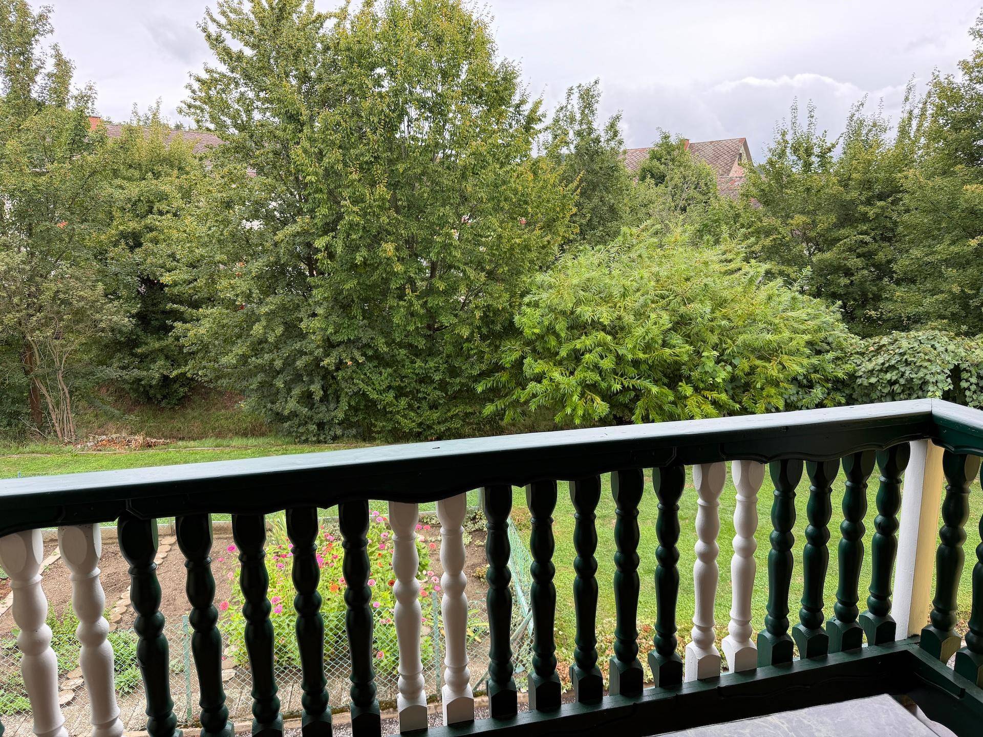 Balkon mit traditionellem Geländer und Blick auf den üppigen grünen Garten und die Umgebung.