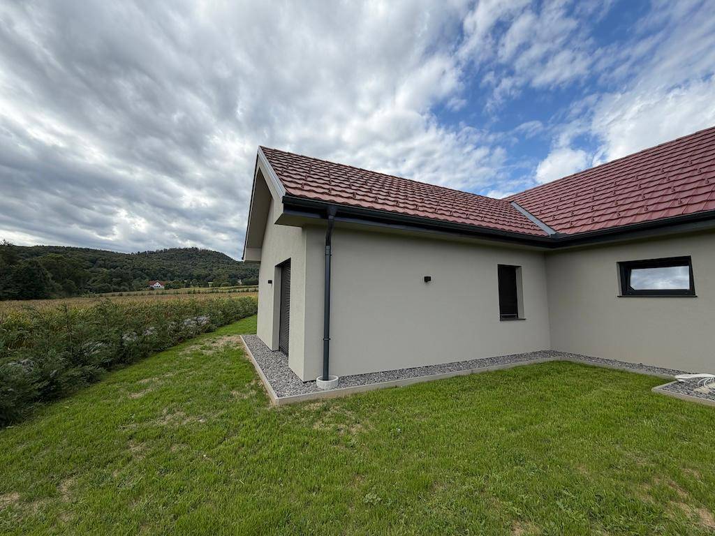 Seitenansicht des Hauses mit Rasenfläche und weitem Blick auf die grüne Landschaft unter blauem Himmel.
