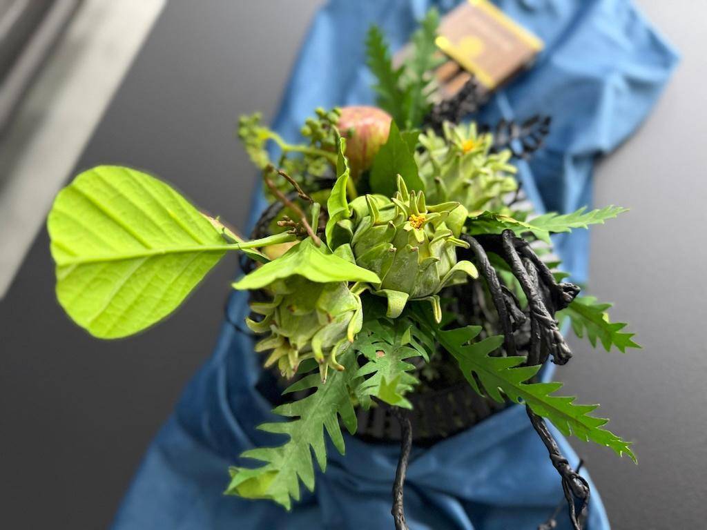Nahaufnahme einer dekorativen Pflanzenanordnung auf einem Tisch mit blauem Stoff im Hintergrund.
