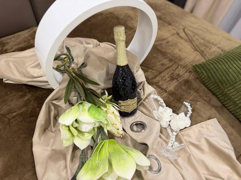 Dekorative Anordnung mit Champagnerflasche, Blumen und Gläsern auf einem Bett.