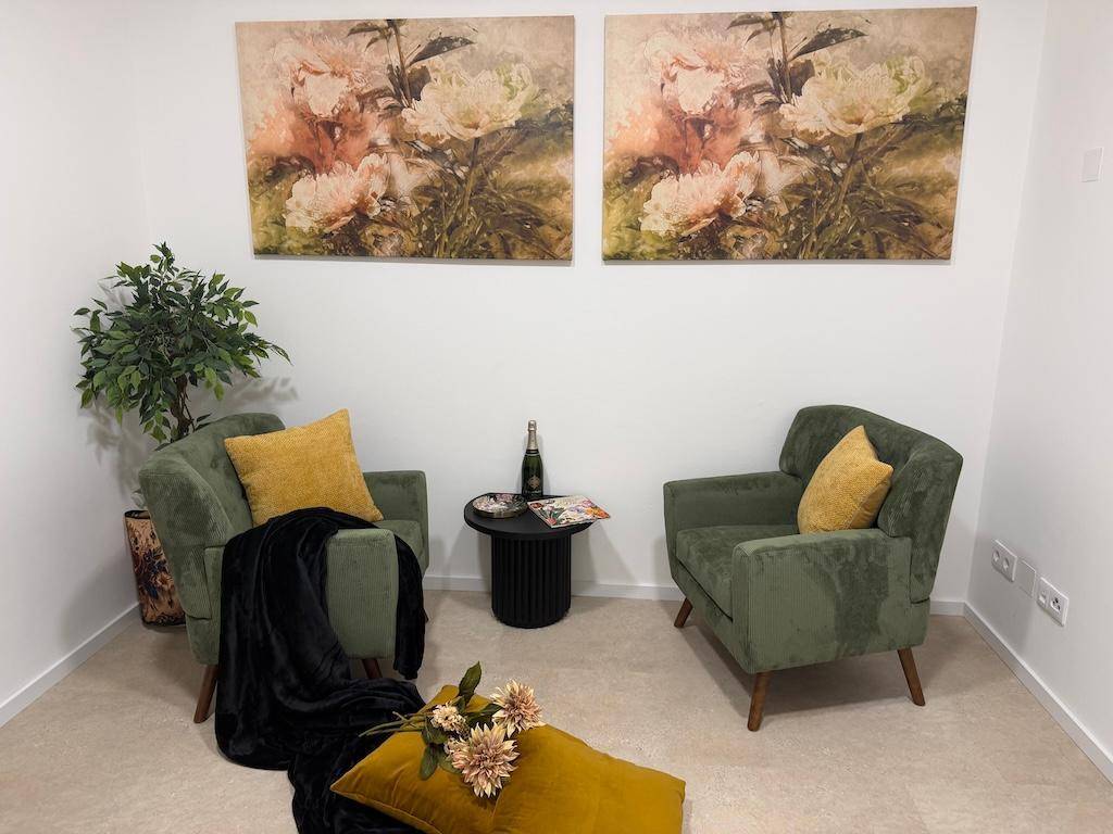 Gemütliche Sitzecke mit zwei grünen Sesseln, Beistelltisch und floralen Wandbildern.