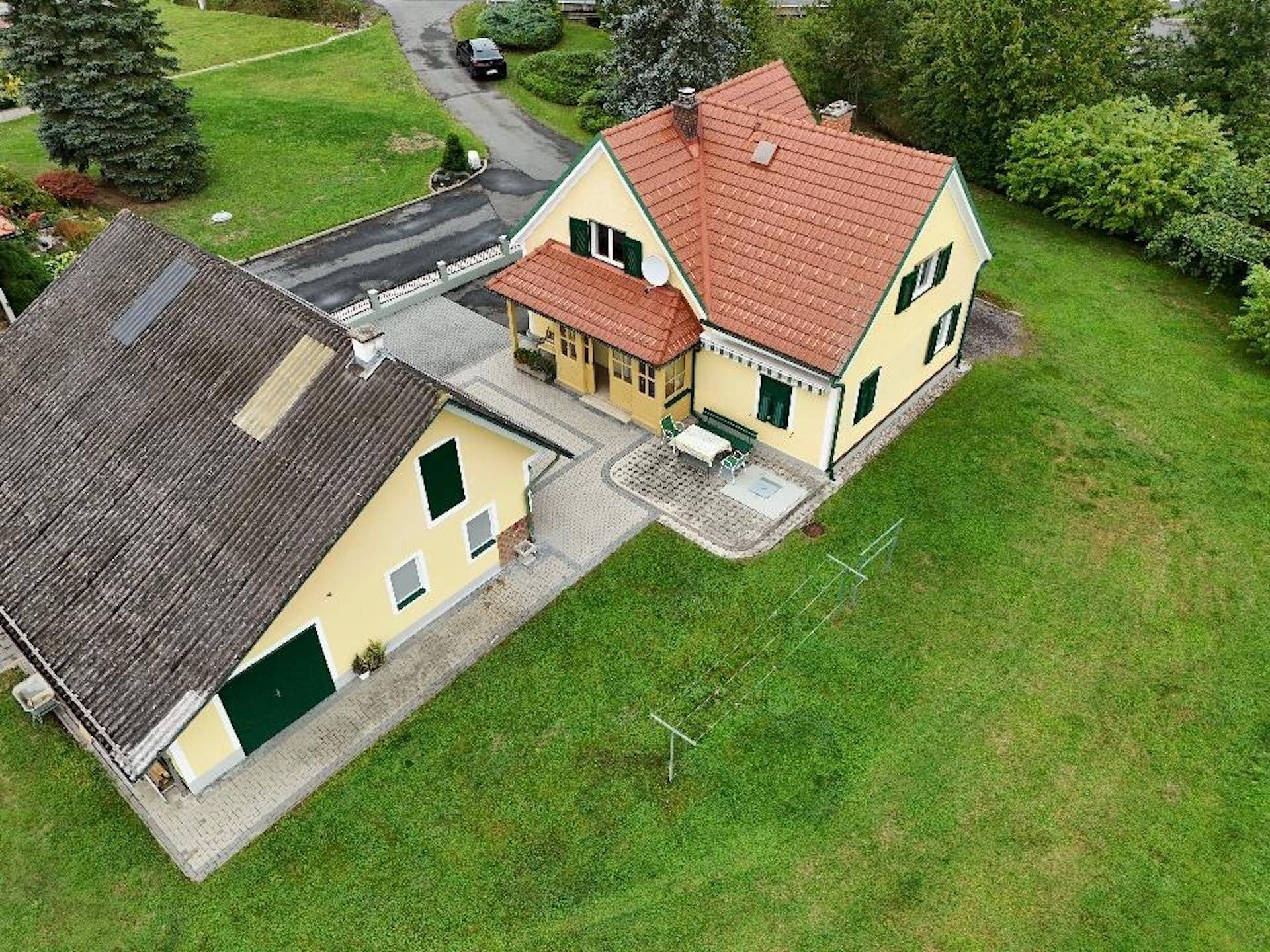 Luftaufnahme des Anwesens mit zwei Gebäuden, großem Rasen und gepflastertem Hofbereich.