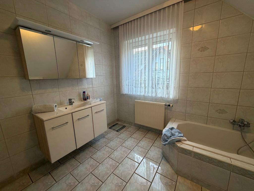 Badezimmer mit Waschtisch, Spiegelschrank, Eckbadewanne und Fenster für Tageslicht.
