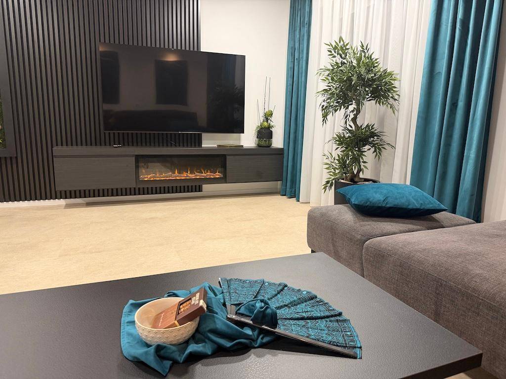 Gemütlicher Wohnbereich mit großem Sofa, Vorhängen in Türkis und einem modernen Couchtisch.