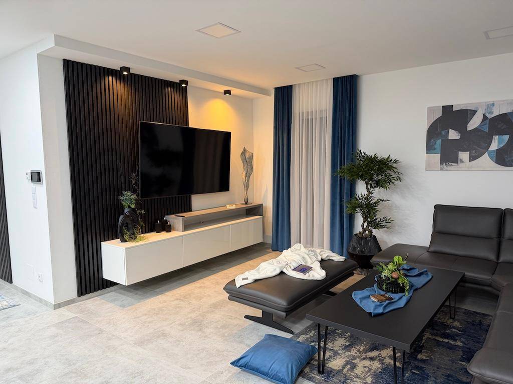 Modernes Wohnzimmer mit großem Fernseher, bequemer Eckcouch und stilvollen blauen Vorhängen.